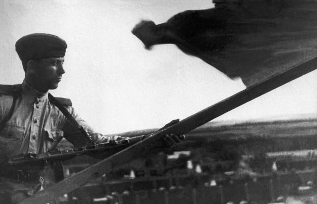 Боец РККА устанавливает красный флаг на крыше дома в одном из населенных пунктов Южного Сахалина. 1945