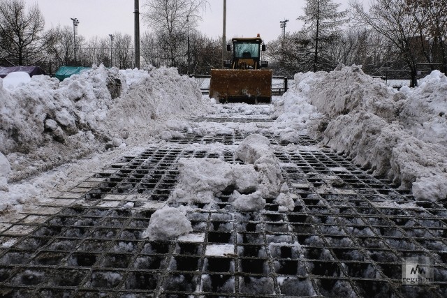 Специальная техника проталкивает снег широкими колесами и ковшом через решетку в канализацию