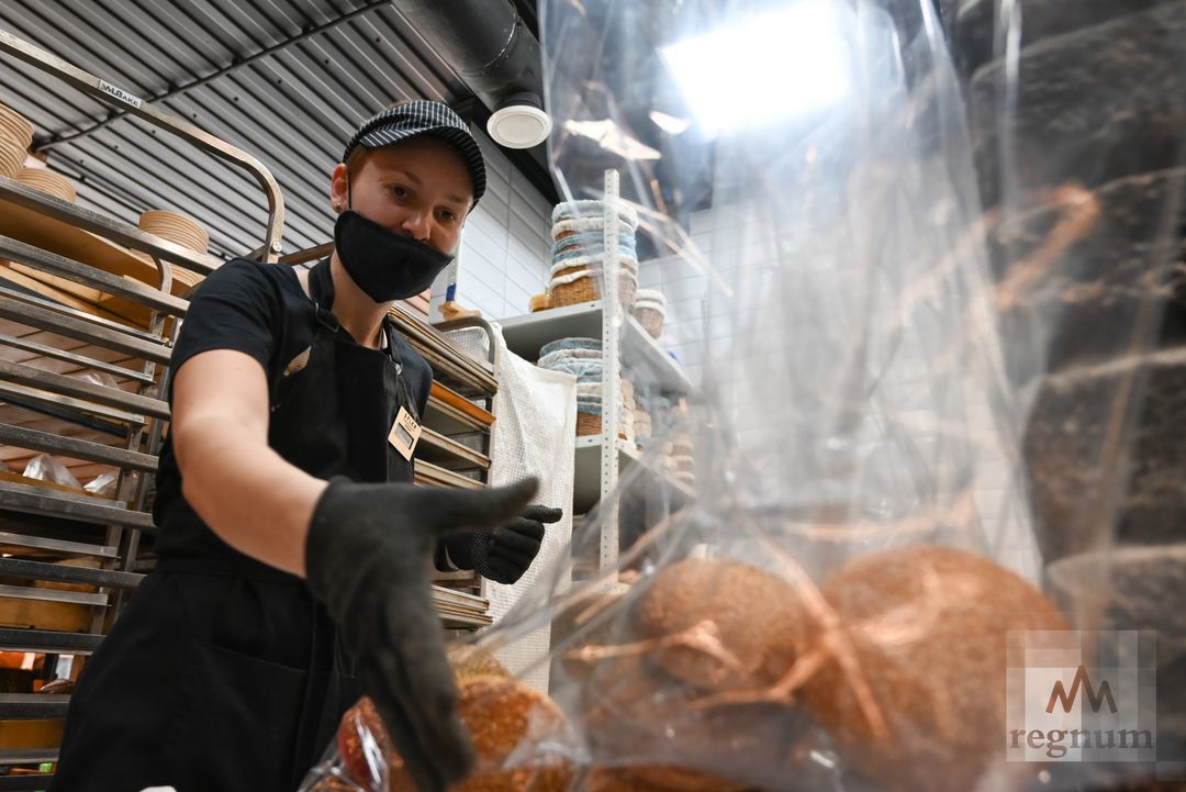 Работник пекарни-буфета упаковывает булки с кунжутом для бургеров