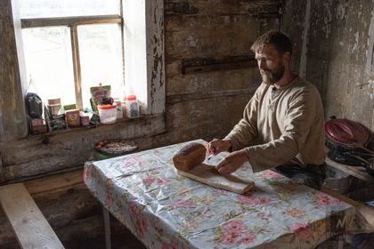 Андрей, профессиональный плотник-реставратор, режет свежий хлеб, которым реставраторов угощают драгировщики.